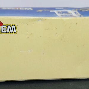 Puede incluir: Una caja blanca con el logotipo de LEGO SYSTEM en rojo y azul. La caja tiene un fondo azul con nubes blancas. La caja es para un set de LEGO.