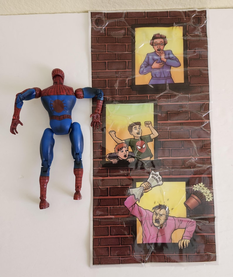 May include: A blue and red Spider-Man action figure stands next to a brick wall backdrop with three illustrated window scenes. The scenes depict people reacting to something, with one holding a newspaper that reads "Spider-Man Menace."