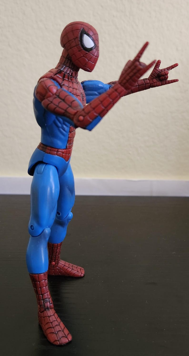 May include: A Spider-Man action figure in a dynamic pose, featuring a red and blue costume. The figure has a red mask with white eye lenses and is striking a hand gesture. The figure is approximately 6 inches tall.
