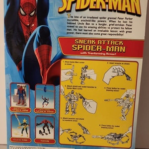 May include: The Amazing Spider-Man action figure with transforming armour. The figure is red and blue with a black spider symbol on the chest. The figure comes with a shield, rocket launcher, and missile. The packaging shows instructions on how to assemble the armour. The packaging also features other Spider-Man characters, including Electro and Toxin.