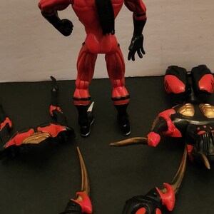 May include: A red and black action figure with a long black ponytail. The figure is standing with its arms outstretched. The figure is surrounded by several black and red pieces of a larger figure.