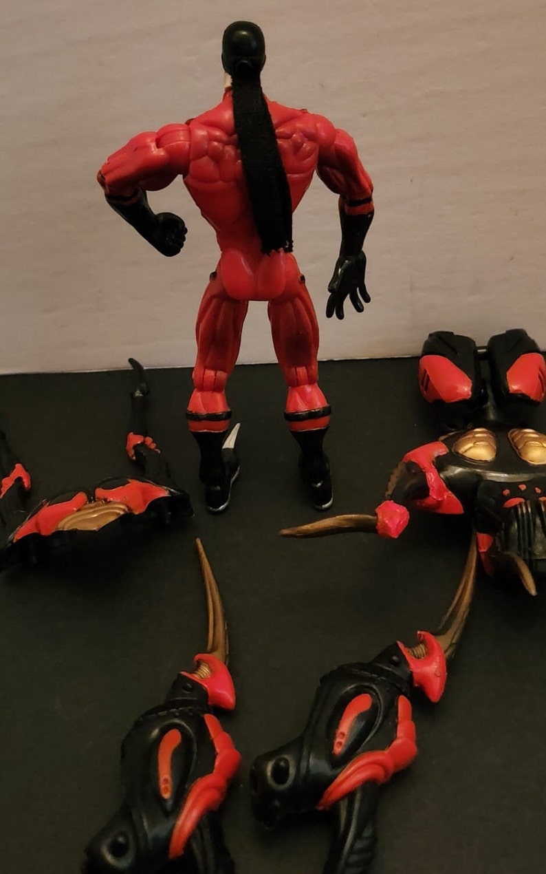 May include: A red and black action figure with a long black ponytail. The figure is standing with its arms outstretched. The figure is surrounded by several black and red pieces of a larger figure.