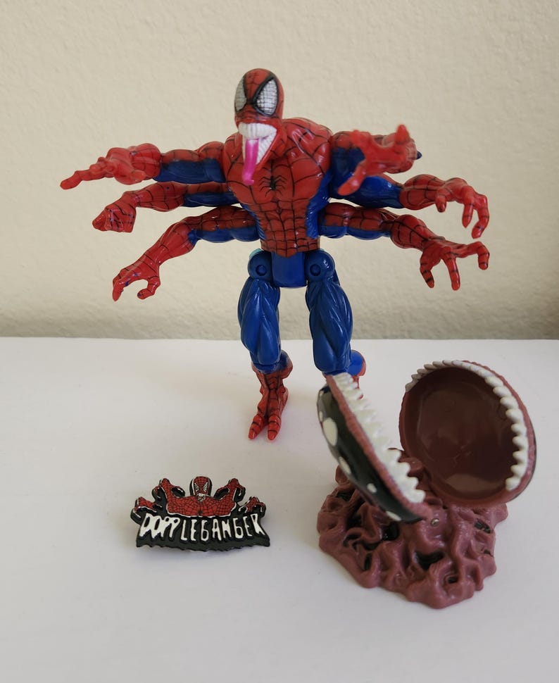 May include: A Spider-Man action figure with six arms, red and blue suit, and a long pink tongue. Includes a small pin with the word "Doppelganger" and a brown, open-mouthed creature.