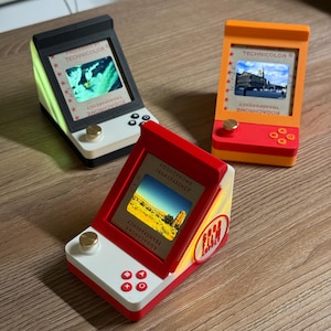 May include: Three desktop light boxes shaped like miniature arcade consoles, each displaying a Kodachrome transparency slide. The units feature a gold-colored knob, directional buttons, and a screen frame labeled with Technicolor and Kodachrome text.