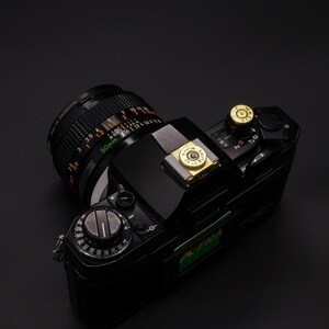 May include: Black vintage camera with a 50mm lens. The camera has a black body with a silver and gold accent. The lens has a black and silver design with the text "50mm" and "UV PROTECTOR USA".
