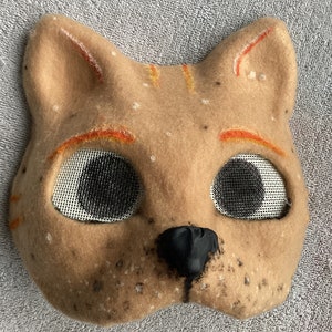 Brown and orange felted cartoon style cat mask with black and white freckles