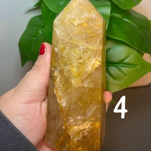 Puede incluir: Una gran punta de cristal de citrino amarillo claro con una superficie rugosa y texturizada. El cristal se sostiene en una mano, y el n&uacute;mero "4" est&aacute; escrito en el fondo.