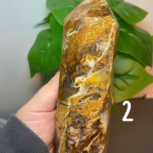 Puede incluir: Una gran punta de cristal de cuarzo de color marr&oacute;n dorado claro con inclusiones blancas y amarillas. El cristal mide aproximadamente 15 cm de alto y tiene una punta puntiaguda. El cristal est&aacute; sentado sobre una superficie marr&oacute;n.