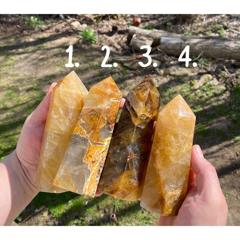 Puede incluir: Cuatro puntas de cristal de citrino dorado, numeradas del 1 al 4, se sostienen en una mano. Los cristales son de varios tonos de amarillo y marr&oacute;n.