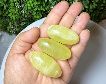May include: Three yellow calcite tumbled stones, each with a smooth, oval shape and a light yellow color.