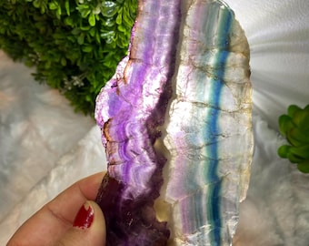 May include: A large, iridescent fluorite crystal with purple, blue, and white banding. The crystal is translucent and has a smooth, polished surface.