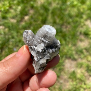 May include: A small cluster of clear, white, and gray crystals on a gray rock. The crystals are clustered together in a natural formation.