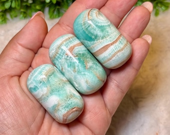 May include: Three polished, cylindrical stones featuring a smooth, glossy finish with swirling patterns of mint green, white, and tan. The stones exhibit a banded, layered appearance with a translucent quality, showcasing natural mineral formations.