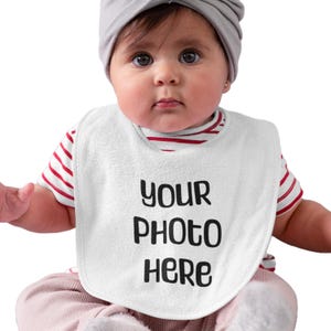 May include: A white baby bib with the text "YOUR PHOTO HERE" in black. The baby is wearing a red and white striped top and a grey turban. The bib is around the baby's neck.