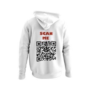 May include: White hoodie featuring the text "SCAN ME" in red above a black QR code. The back of the sweatshirt is visible. The hoodie has a drawstring and a kangaroo pocket. The design is printed on the back.