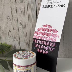 May include: A jar of "Sugared Pink" stencil butter frosting beside a card with a pink leaf design. The jar has a white lid and a label that reads "Stencil Butter Frosting" and "Sugared Pink". The card has the same text and design.