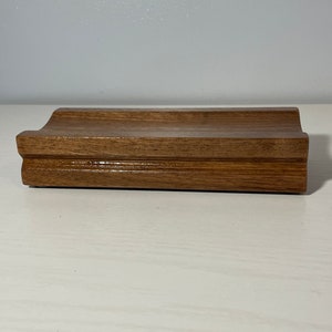 May include: A wooden soap dish with a curved design. The dish is made of dark brown wood and has a smooth, polished finish.