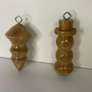 May include: Two wooden Christmas ornaments. One is a teardrop shape with a textured surface. The other is a snowman shape with a hat. Both have a silver wire loop for hanging.