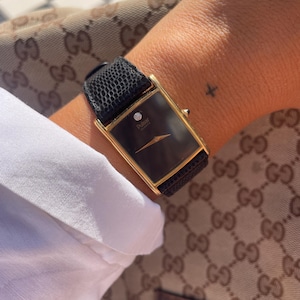 Könnte beinhalten: Eine rechteckige Pulsar-Quarzuhr mit goldfarbenem Gehäuse, schwarzem Zifferblatt mit einem einzelnen Diamantakzent auf der Zwölf-Uhr-Position und einem strukturierten schwarzen Lederarmband mit Eidechsenhautmuster.