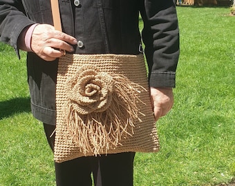 May include: A tan crocheted bag with a large flower design. The bag has a long strap and is worn over the shoulder.