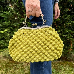 May include: A bright yellow crocheted purse with a vintage-style metal clasp and handle.