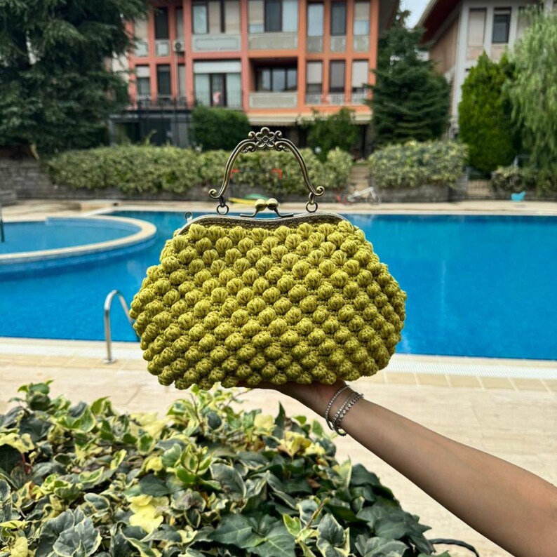 May include: A bright green crocheted purse with a vintage-style clasp and a metal handle. The purse is made of small, round stitches and has a textured appearance.