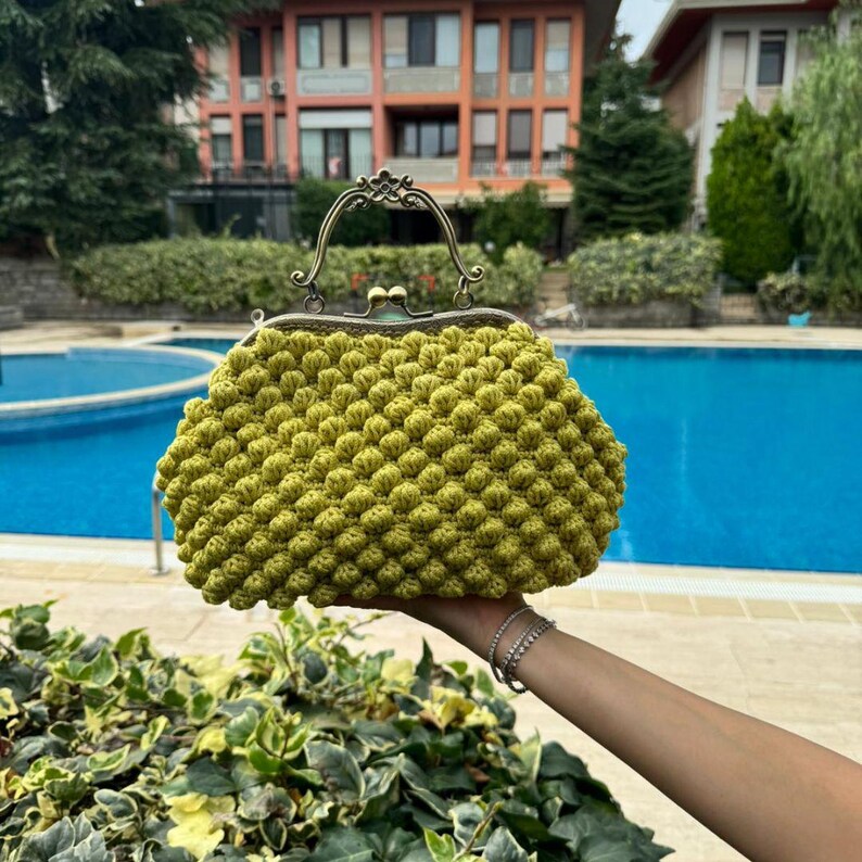 May include: A lime green crocheted purse with a vintage-style metal clasp and handle. The purse is made of small, round crocheted stitches.