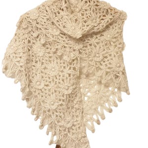 May include: A white crocheted shawl with a floral pattern. The shawl has a scalloped edge and is made of a soft, lightweight yarn.