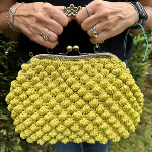 May include: A yellow crocheted purse with a vintage-style metal clasp and a flower-shaped handle.