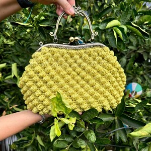 May include: A crocheted handbag with a yellow, textured, bubble-like design. The bag has a silver metal frame with a top handle.