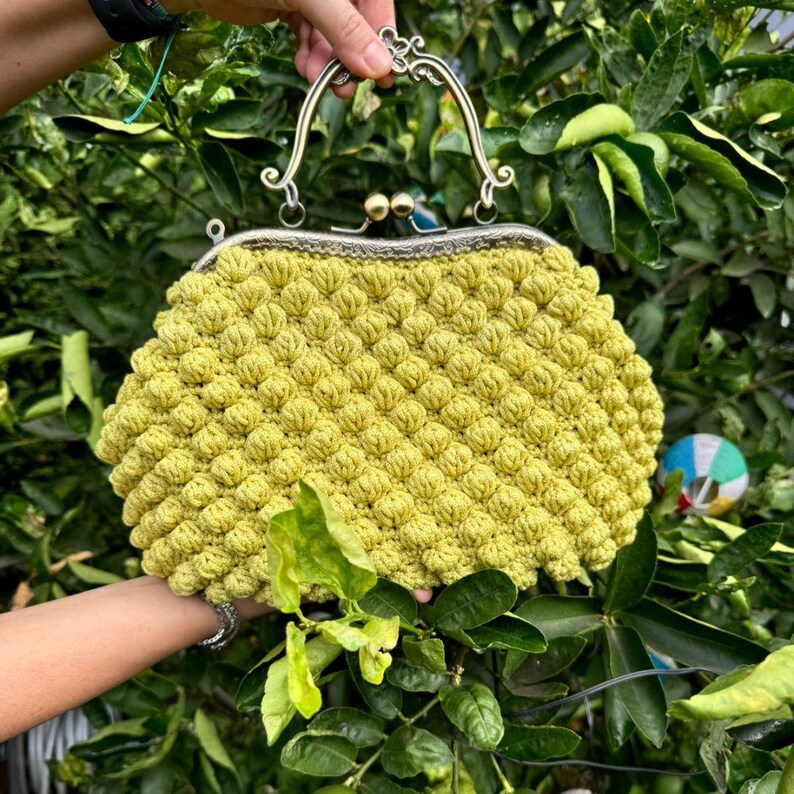 May include: A crocheted handbag with a yellow, textured, bubble-like design. The bag has a silver metal frame with a top handle.