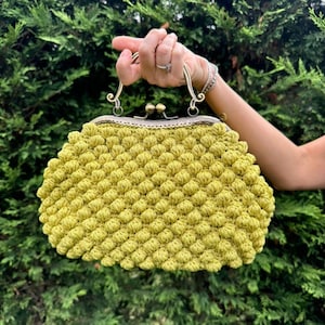 May include: A bright yellow crocheted purse with a vintage-style metal clasp and handle.