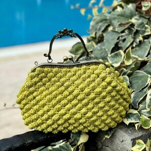 May include: A lime green crocheted clutch purse with a vintage-style brass clasp and handle.