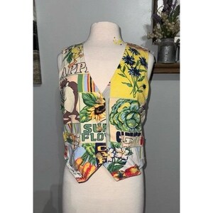 May include: A patchwork vest featuring cartoon characters, sunflowers, and the text "SUN FLOWERS". The vest has a V-neck and is displayed on a mannequin. The vest's design includes various colors and patterns.