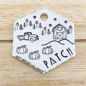 May include: A silver metal tag with a hand-drawn design featuring a truck, pumpkins, trees, a barn, and the word "PATCH". The tag has a hole at the top for hanging and a textured edge. The design is in black.
