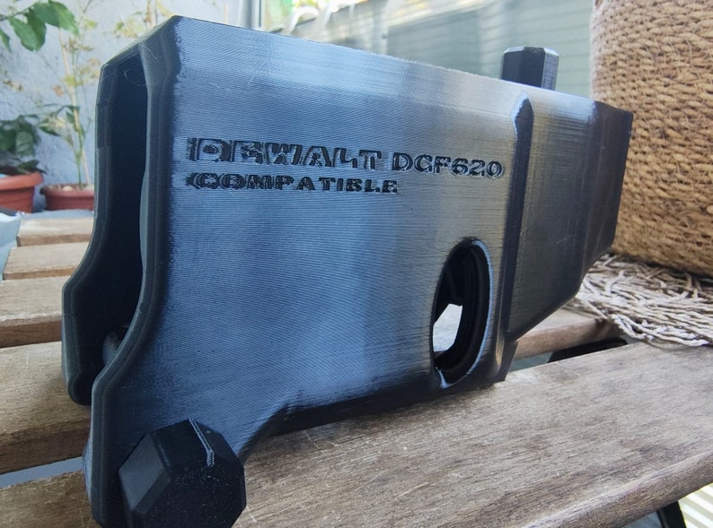 Puede incluir: Pieza de pl&aacute;stico negro impresa en 3D para un taladro DeWalt DCF620. La pieza es compatible con el taladro y tiene una superficie texturizada.