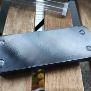 Puede incluir: Objeto rectangular negro con cuatro c&iacute;rculos redondos transparentes en la superficie superior. El objeto est&aacute; hecho de un material texturizado.