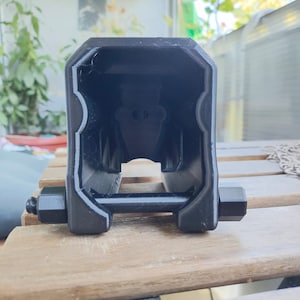 Puede incluir: Un objeto de pl&aacute;stico negro impreso en 3D con una abertura rectangular y dos pernos met&aacute;licos a cada lado.