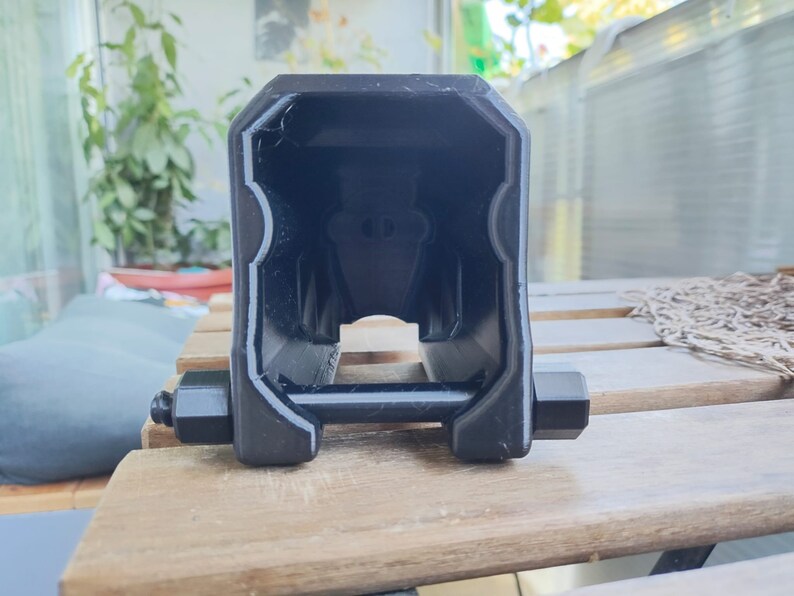 Puede incluir: Un objeto de pl&aacute;stico negro impreso en 3D con una abertura rectangular y dos pernos met&aacute;licos a cada lado.