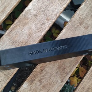 Puede incluir: Un objeto rectangular negro con el texto "MADE IN CROATIA" en relieve en la parte superior. El objeto est&aacute; sobre una superficie de madera.