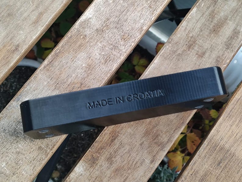 Puede incluir: Un objeto rectangular negro con el texto "MADE IN CROATIA" en relieve en la parte superior. El objeto est&aacute; sobre una superficie de madera.