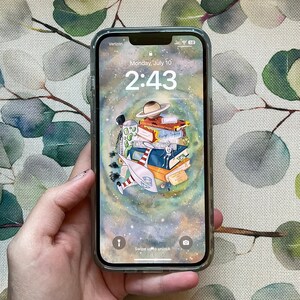 May include: A smartphone displaying a colorful illustration of a rocket ship flying through space with a stack of books. The time is 2:43 and the date is Monday, July 10. The phone is in a clear case.