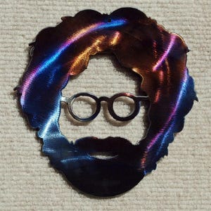 May include: A metal cutout of a person with long hair, glasses, and a beard. The metal is a dark blue and purple color with a rainbow sheen.