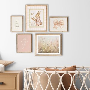 May include: Five framed prints on a white wall, including a watercolor illustration of a bunny reading a book, a floral print, a print with the text "you are loved", a print with the text "hello beautiful little you", and a print of a pink bow.