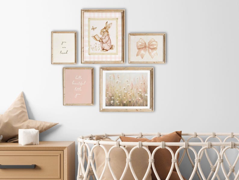 May include: Five framed prints on a white wall, including a watercolor illustration of a bunny reading a book, a floral print, a print with the text "you are loved", a print with the text "hello beautiful little you", and a print of a pink bow.