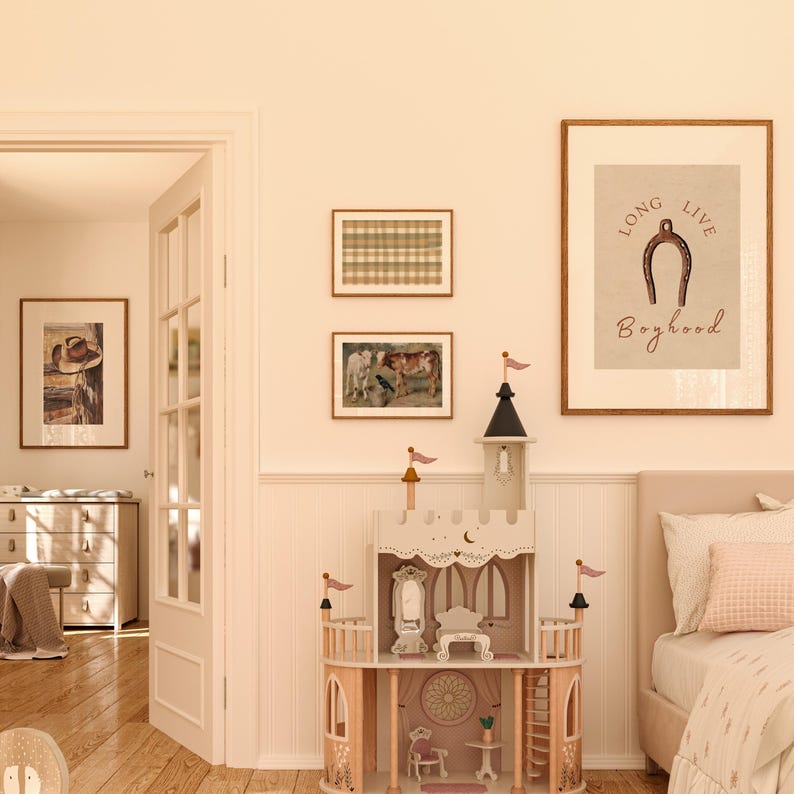 May include: A light brown wooden dollhouse with a white roof and pink accents. The dollhouse has a large window and a small door. The dollhouse is sitting on a light brown wooden floor. There is a framed print on the wall behind the dollhouse that says "Long Live Boyhood" with a horseshoe illustration.