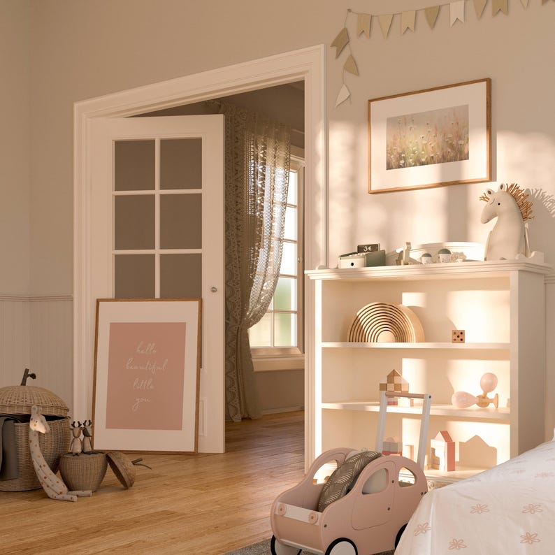 May include: A white bookshelf with three shelves, filled with toys and books. The top shelf has a rainbow wooden toy, a small wooden box, and a white unicorn figurine. The middle shelf has a wooden toy, a small wooden box, and a wooden toy. The bottom shelf has a pink toy car, a wooden toy, and a small wooden house. The bookshelf is in a room with a white door and a window with a white curtain. The room has a light brown wooden floor. The wall is painted a light beige color. There is a framed picture on the wall above the bookshelf. The picture is of a field of flowers. There is a sign on the wall that says "Little beautiful little you".
