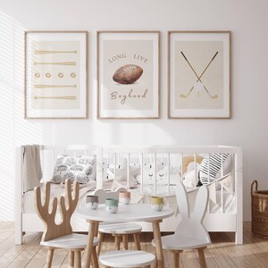 May include: Three framed prints with a sports theme. The left print features a beige background with brown baseball bats and balls. The center print has a beige background with a brown football and the text "Long Live Boyhood". The right print has a beige background with two brown golf clubs crossed over a white golf ball.