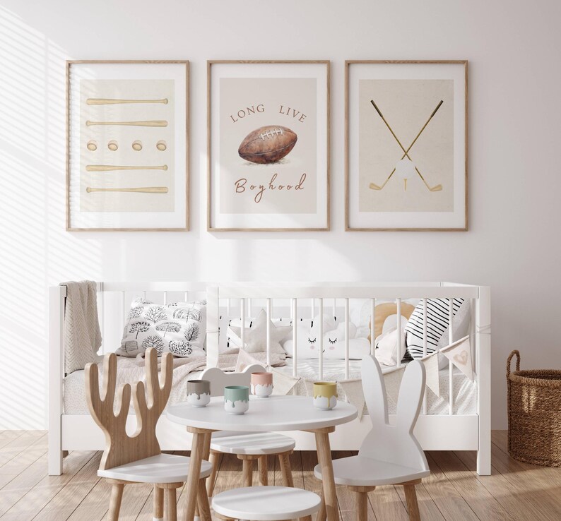 May include: Three framed prints with a sports theme. The left print features a beige background with brown baseball bats and balls. The center print has a beige background with a brown football and the text "Long Live Boyhood". The right print has a beige background with two brown golf clubs crossed over a white golf ball.