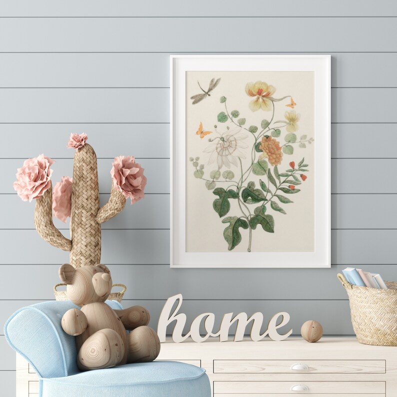 May include: A framed botanical print featuring a detailed illustration of flowers, leaves, and insects in shades of yellow, orange, and green. A woven cactus with pink flowers, a wooden bear, and the word "home" are also visible.